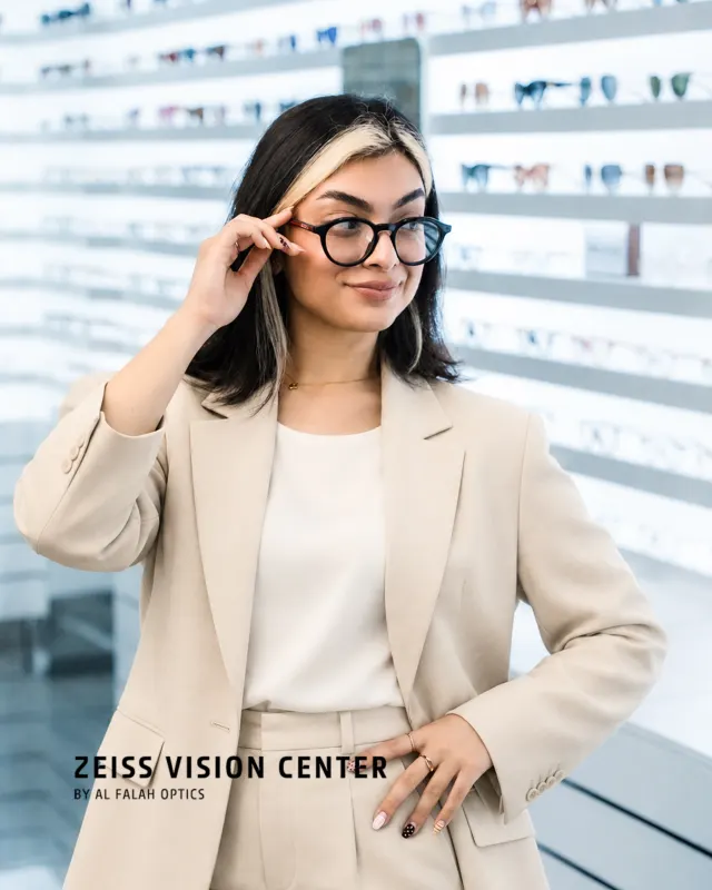 Woman adjusting her glasses in front of a frame wall at ZEISS Vision Center